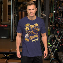 Load image into Gallery viewer, A man wearing the Happy Cookies Premium Unisex T-Shirt in the colour heather midnight navy, featuring a graphic of ten different types of cookies with smiling faces