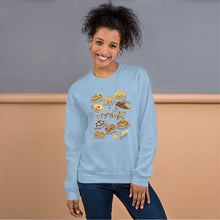 Load image into Gallery viewer, A woman is wearing the Happy Cookies Unisex Sweatshirt in the colour light blue, which features a print of 10 different types of cookies with smiley faces