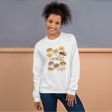 Load image into Gallery viewer, A woman is wearing the Happy Cookies Unisex Sweatshirt in the colour white, which features an illustration of 10 different types of cookies with smiley faces