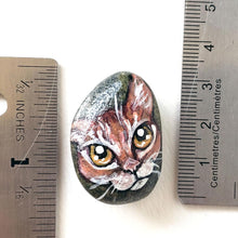 Load image into Gallery viewer, a small beach rock painted with of an orange tabby cat with golden yellow eyes, available as either a keepsake or a pendant necklace
