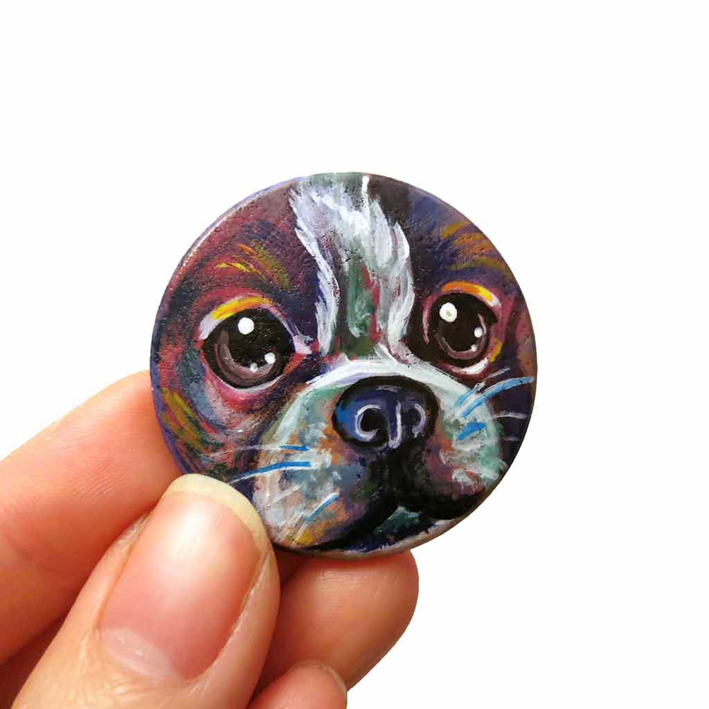 a wood disc is hand painted with a portrait of a boston terrier dog in rainbow colours. it's available as a wood keepsake or pendant necklace