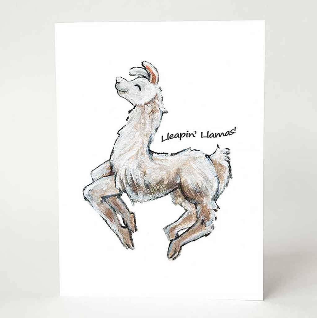 A greeting card, printed with an illustration of a smiling white and brown llama jumping, with the words 