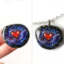 Load image into Gallery viewer, a beach stone has been hand painted with a heart surrounded by outer space and stars, and hand crafted as either a keepsake stone, magnet, or pendant necklace
