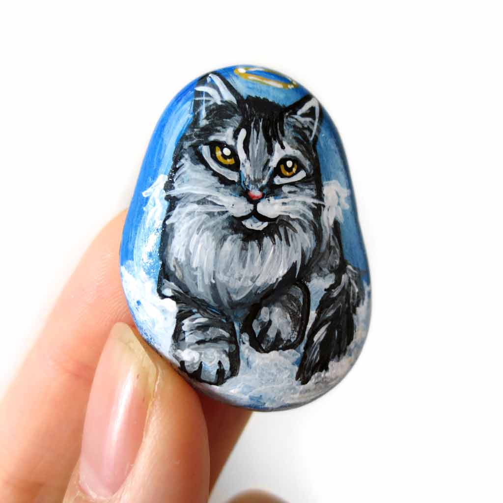 art of a silver gray maine coon cat as an angel, is hand painted on a river rock, and is available as either a keepsake, magnet or a pendant necklace