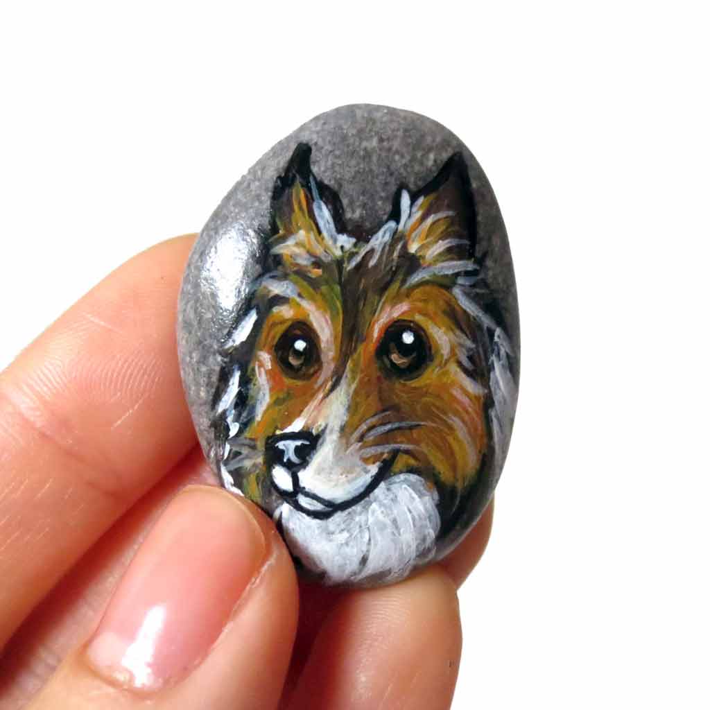a beach rock painted with dog art: a portrait of a rough collie, available as either a keepsake, fridge magnet, or a pendant necklace