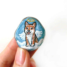 Load image into Gallery viewer, a smooth beach stone, hand painted with a portrait of a shiba inu dog as an angel, sitting on clouds against a light blue sky. available as a keepsake or pendant necklace
