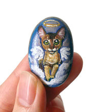 Load image into Gallery viewer, art of an Abyssinian cat, painted as an angel in the clouds. hand painted on a beach stone, available as a keepsake or pendant necklace
