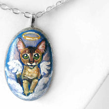 Load image into Gallery viewer, art of an Abyssinian cat, painted as an angel in the clouds. hand painted on a beach stone, available as a keepsake or pendant necklace
