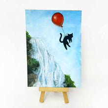 Load image into Gallery viewer, 5x7&quot; original painting on a small easel: a black cat floats in the sky, tied to a red balloon, the cat soars over a waterfall, against a blue sky
