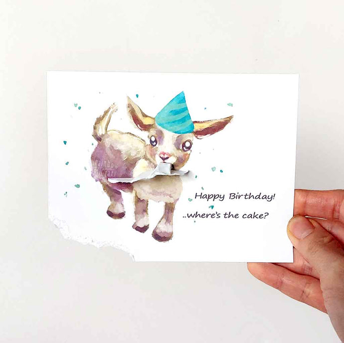 a greeting card featuring an illustration of a baby goat wearing a blue birthday hat, with the bottom left corner of the card hanging from its mouth. The card reads, Happy Birthday! .. where's the cake?