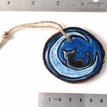 Load image into Gallery viewer, a wood slice ornament, hand painted with the silhouette of a black cat, curled up on a crescent moon, against a dark blue background
