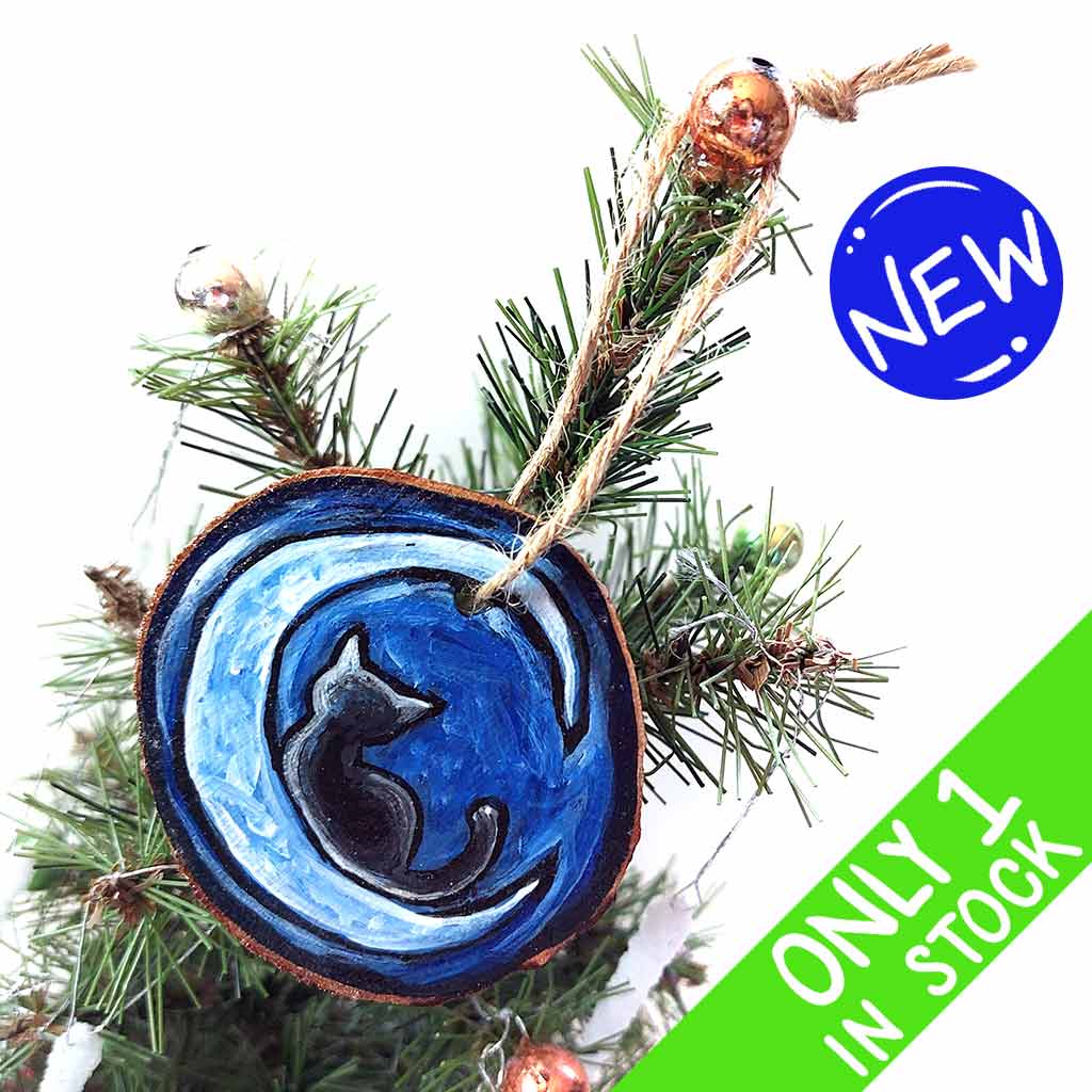 a wood slice ornament, hand painted with the silhouette of a black cat, curled up on a crescent moon, against a dark blue background