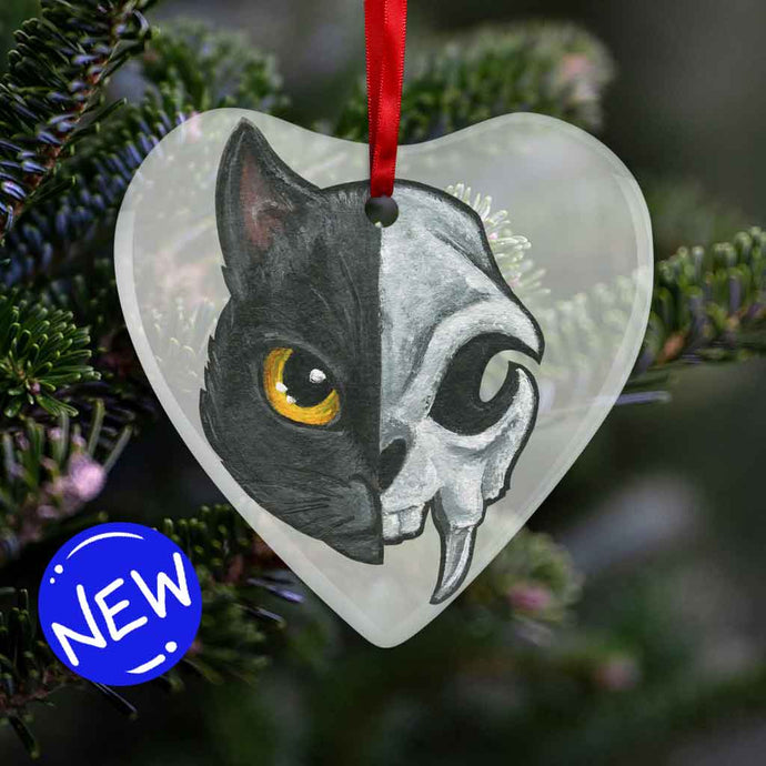 a heart shaped glass ornament, featuring an illustration of a black cat’s portrait. the left side features the cat’s face, while the right side features a stylized cat skull
