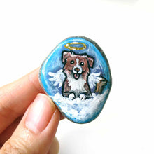 Load image into Gallery viewer, a small beach stone, hand painted with the portrait of a smiling Australian Shepherd dog, as an angel with wings and halo, sitting on fluffy clouds against a blue sky. this piece is available as a stone keepsake or pendant necklace
