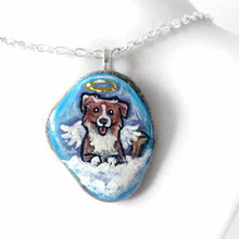 Load image into Gallery viewer, a small beach stone, hand painted with the portrait of a smiling Australian Shepherd dog, as an angel with wings and halo, sitting on fluffy clouds against a blue sky. this piece is available as a stone keepsake or pendant necklace
