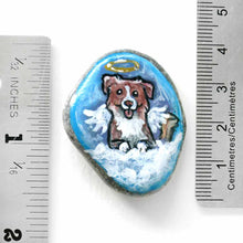 Load image into Gallery viewer, a small beach stone, hand painted with the portrait of a smiling Australian Shepherd dog, as an angel with wings and halo, sitting on fluffy clouds against a blue sky. this piece is available as a stone keepsake or pendant necklace
