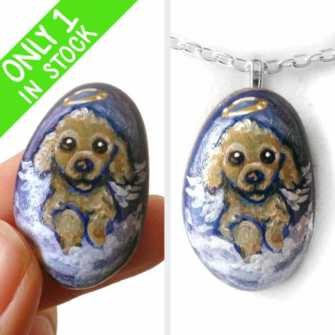 a small beach stone hand painted with the portrait of a brown poodle as an angel, sitting in the clouds against a blue sky. available as a keepsake or pendant necklace