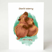 Load image into Gallery viewer, a greeting card with an illustration of two capybaras hugging. the front of the card reads &quot;Don&#39;t Worry Be Capy&quot;
