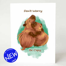 Load image into Gallery viewer, a greeting card with an illustration of two capybaras hugging. the front of the card reads &quot;Don&#39;t Worry Be Capy&quot;
