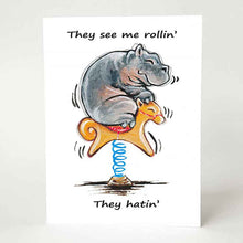 Load image into Gallery viewer, a greeting card with a smiling hippo, riding an orange rocking horse. the card reads, &quot;they see me rollin&#39;. they hatin&#39;&quot;
