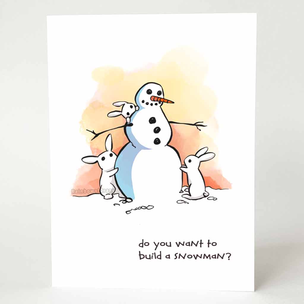 greeting card with an illustration of a smiling snowman with three small white rabbits helping to build it. on the bottom, the card says, 
