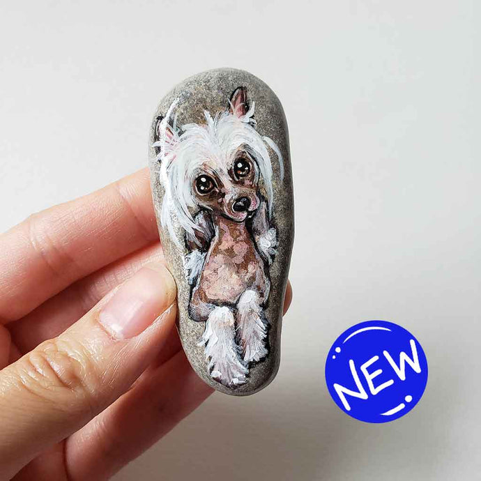 a small beach stone, hand painted with the portrait of a chinese crested dog