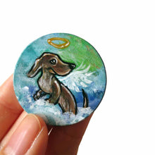 Load image into Gallery viewer, a lightweight wood disc, hand painted with the portrait of a dachshund, as an angel, sitting on fluffy clouds against a green and blue sky. available as a keepsake or pendant necklace 
