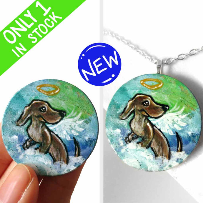 a lightweight wood disc, hand painted with the portrait of a dachshund, as an angel, sitting on fluffy clouds against a green and blue sky. available as a keepsake or pendant necklace 