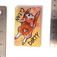 Load image into Gallery viewer, yellow and orange wood magnet, hand painted with a corgi with a tail in a heart shape, tongue out, doing a sploot. near the top of the dog&#39;s head is the word CLEAN. written reversed, next to the dog&#39;s butt is the word DIRTY
