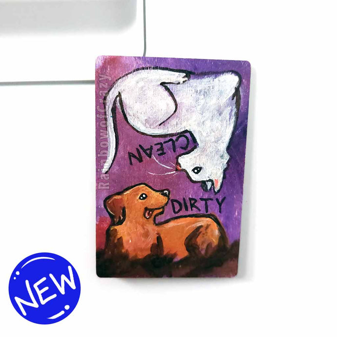 wood magnet on a dishwasher, hand painted with a white cat with the word CLEAN next to it. at the top, upside down, is a Golden labrador dog that is covered in mud, with word DIRTY next to it, background a purple colour