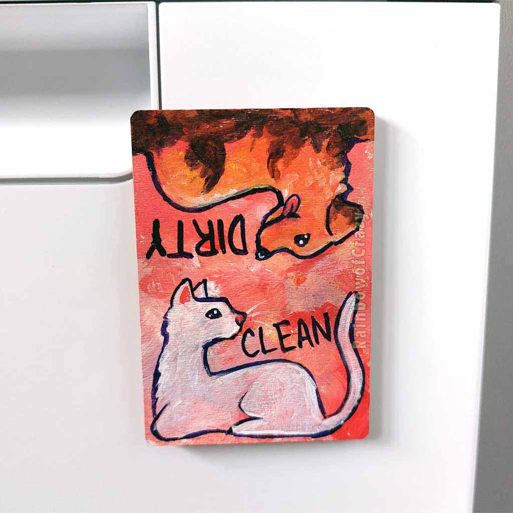 wood magnet on a dishwasher, hand painted with a white cat with the word CLEAN next to it. at the top, upside down, is a Golden labrador dog that is covered in mud, with word DIRTY next to it. background is a soft red colour