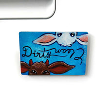 Load image into Gallery viewer, blue wood magnet, hand painted, bottom features a brown goat with little red horns with the word &quot;Dirty&quot; above them. at the top, upside down is a white goat, with the word &quot;clean&quot; above them
