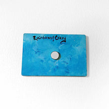 Load image into Gallery viewer, back of a blue wood magnet, with a small magnet in the center. signed with &quot;RainbowofCrazy&quot;

