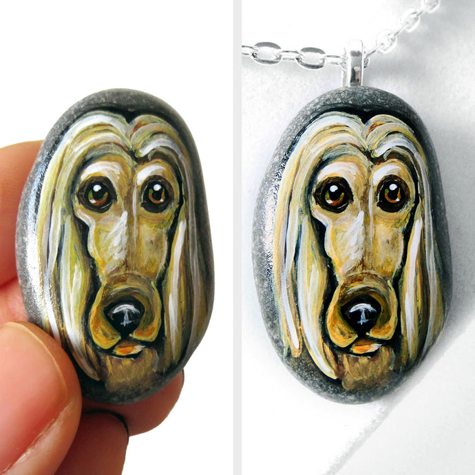 a small beach stone, hand painted with a portrait of an Afghan Hound dog, available as a keepsake stone or necklace.