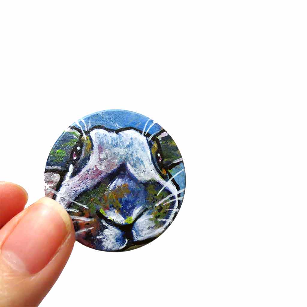 a small round wood disc, hand painted with a portrait of an English Spot rabbit, face up close, painted in rainbow colours. it's available as a keepsake or pendant necklace