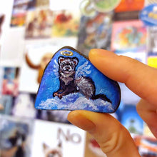 Load image into Gallery viewer, a small beach stone, painted with a portrait of a ferret as an angel in the clouds
