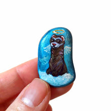 Load image into Gallery viewer, a small beach stone, painted with a smiling ferret angel, with halo and wings, on top of clouds, against a blue sky. available as a keepsake, magnet or pendant necklace
