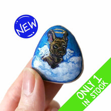 Load image into Gallery viewer, a small beach stone, hand painted with a portrait of a brindle french bulldog, as an angel in the clouds. 
