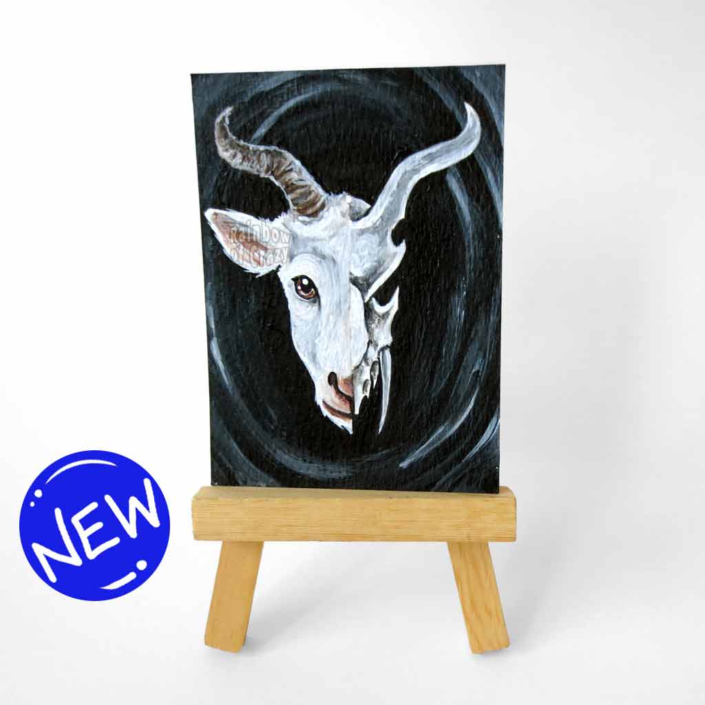 an aceo features a split image: a white horned goat's head on the left side, and a darker, stylized goat skull on the right