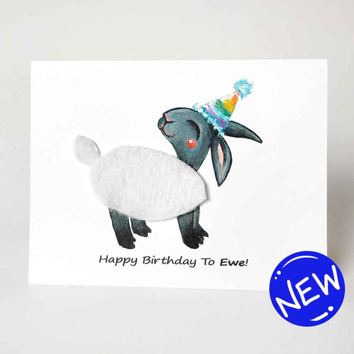 a greeting card featuring an illustration of a smiling black sheep with white fleece, wearing a rainbow party hat. its fleece is made with real fleece fabric. the front reads, 