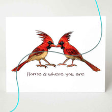 Load image into Gallery viewer, a greeting card featuring an illustration of two cardinals, beaks just touching. it reads, &quot;Home is where you are&quot;. the image has a flowing line through the card, showing colour options of red (male) cardinals or tan (female) cardinals
