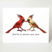 Load image into Gallery viewer, a greeting card featuring an illustration of two cardinals, one male, one female, beaks just touching. it reads, &quot;Home is where you are&quot;.
