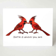 Load image into Gallery viewer, a greeting card featuring an illustration of two cardinals, both male, beaks just touching. it reads, &quot;Home is where you are&quot;.
