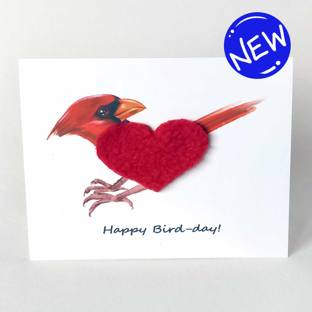 a greeting card with an illustration of a cardinal, its body made from soft red fleece fabric, cut into the shape of a heart. the card reads, 