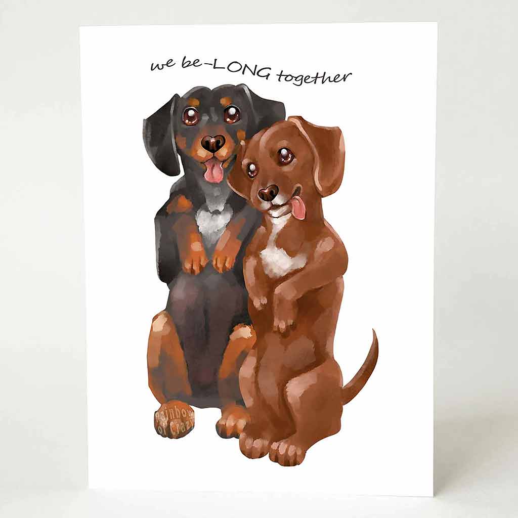 a greeting card with an illustration of one black dachshund, and one brown dachshund, both standing up on their hind legs. it reads, 