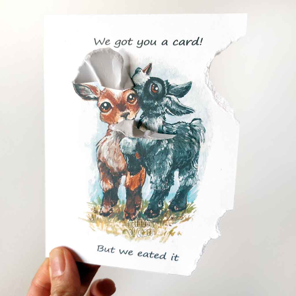 a funny greeting card with two goats: a brown goat and a black goat, on the front, with the piece from the top right, and piece from the bottom right corner of the card ripped and hanging from their mouths. the card reads, 