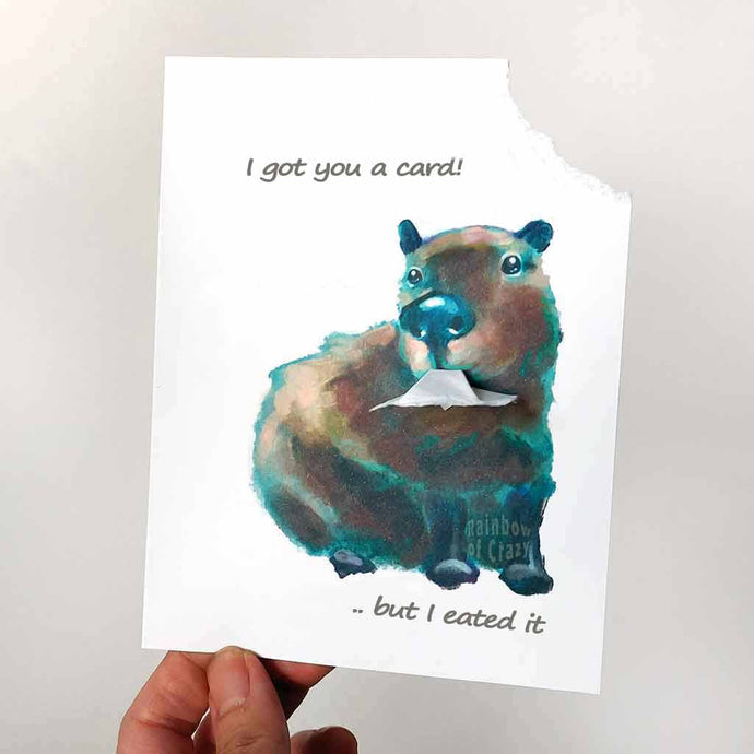 a greeting card illustrated with a capybara. the top right corner of the card has been ripped out and hangs from the capybara's mouth. the card says 