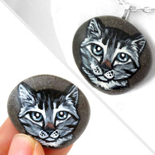 Load image into Gallery viewer, a small beach rock featuring a painting of a grey tabby cat with blue / grey eyes, available as either a keepsake, fridge magnet, or a pendant necklace
