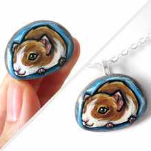 Load image into Gallery viewer, a small beach stone hand painted with a portrait of a guinea pig against a blue background. Available as a keepsake stone or pendant necklace
