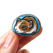 Load image into Gallery viewer, a small beach stone hand painted with a portrait of a guinea pig against a blue background. Available as a keepsake stone or pendant necklace
